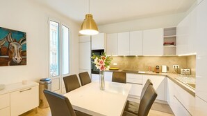 Een moderne keuken met witte kastjes, een eettafel met stoelen, een hanglamp en een vaas met bloemen.