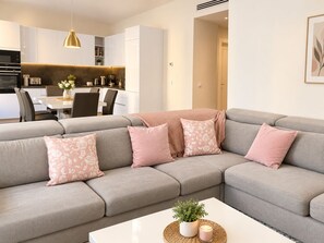 A modern living room with a grey sectional sofa, a white coffee table, and a kitchen in the background.