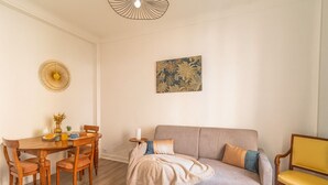 En stue med en sofa, et spisebord med stole, en gul armstol og en vægmonteret lampe.