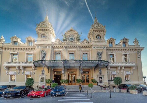 A grand hotel with ornate architecture, a prominent entrance, and a parking area with luxury cars.
