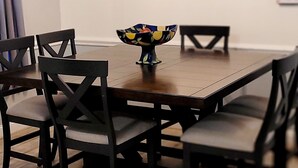 Un comedor con una mesa de madera, seis sillas y un cuenco decorativo. Tres lámparas colgantes iluminan la mesa.