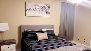 Un dormitorio con cama, mesita de noche, ventilador de techo y un cuadro colgado en la pared.