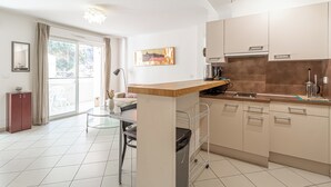 A modern kitchen with a central island, a dining area with a table and chairs, and a view of the outside through a sliding glass door. - 1 bedroom apartment • Near Monaco Train Station (Beausoleil)