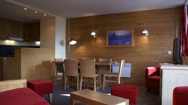 Une pièce chaleureuse avec un mur en bois, une table à manger avec des chaises, un canapé rouge et une petite table.