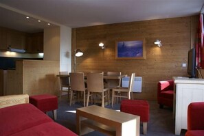 Una habitación acogedora con pared de madera, una mesa de comedor con sillas, un sofá rojo y una mesita.