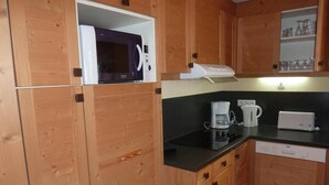 Une cuisine compacte dotée d’armoires en bois, d’un four à micro-ondes, d’une machine à café et d’un grille-pain.