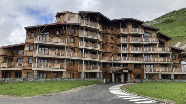 A multi-story wooden building with balconies, a stone base, and a sign reading "ARIETIS."