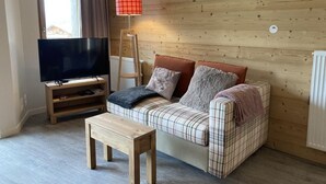 A cozy living room with a plaid sofa, a wooden coffee table, and a flat-screen TV on a stand.