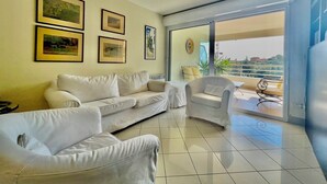 A living room with a white sofa, a chair, and a balcony with a view. - 2 rooms in luxury residence bordering Monaco (Beausoleil)