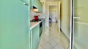 A narrow hallway with a kitchen area on the left, featuring teal cabinets and a red kettle on the stove. - 2 rooms in luxury residence bordering Monaco (Beausoleil)