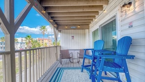 Une véranda couverte avec une balustrade en bois, deux fauteuils Adirondack bleus, une petite table et un tapis.