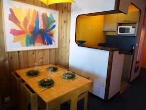 Quarto compacto com mesa de jantar de madeira para quatro pessoas, micro-ondas e pequena cozinha.