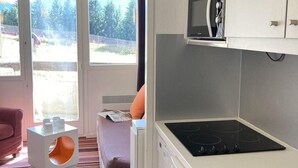 Uma cozinha compacta com micro-ondas, fogão e pia. Há uma janela com vista para árvores e um carro estacionado lá fora.