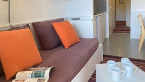 Quarto de hotel moderno com sofá, televisão de tela plana, pequena cozinha e mesa de jantar com xícaras.