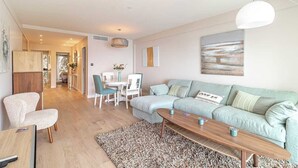 A modern living room with a light blue sofa, a wooden coffee table, and a patterned rug. There is a dining area with a white table and chairs, and a kitchen visible in the background. - magnificent 2-room apartment  sea view Roquebrune (Roquebrune-Cap-Martin)