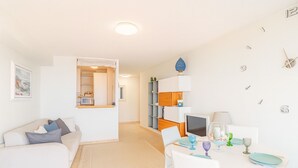 A modern, well-lit living room with a white sofa, a dining table with chairs, and a kitchen area in the background. - Beautiful apartment near Monaco (Beausoleil)