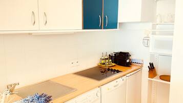 A compact kitchen with white cabinets, a blue door, a microwave, a coffee maker, and a knife block.