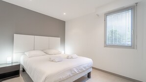 A modern bedroom with a large bed, a bedside table, a headboard, and a window with blinds.