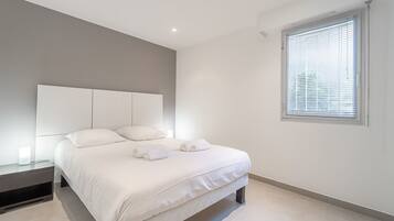 Une chambre à coucher moderne avec un grand lit, une table de chevet, une tête de lit et une fenêtre avec des stores.