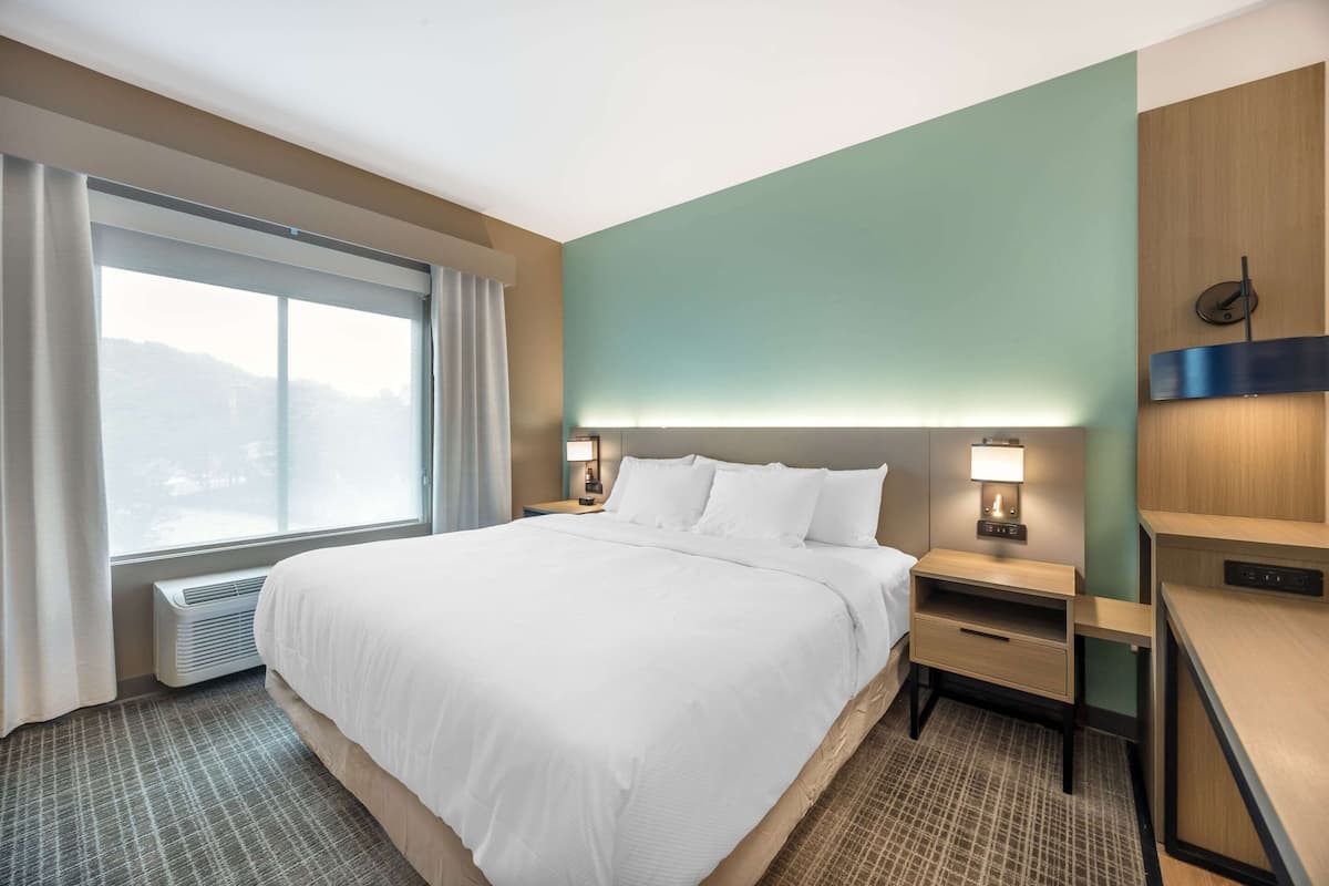 Une chambre d’hôtel avec un grand lit, des tables de chevet, un bureau et une fenêtre avec des rideaux.