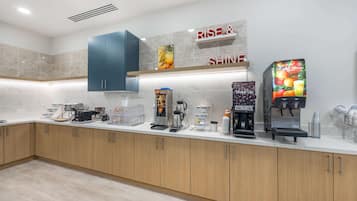 Une cuisine moderne dotée de plans de travail en marbre, d’armoires en bois et d’un espace dédié au café, comprenant plusieurs machines à café et un distributeur de café de marque.