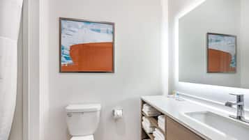 Une salle de bain moderne avec des toilettes, un lavabo et un grand miroir. On y trouve des serviettes sur une étagère et un tableau abstrait encadré au mur.