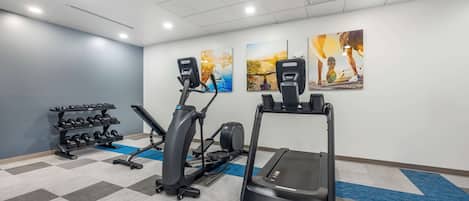 Un gimnasio con cintas de correr, elípticas y un estante con mancuernas.