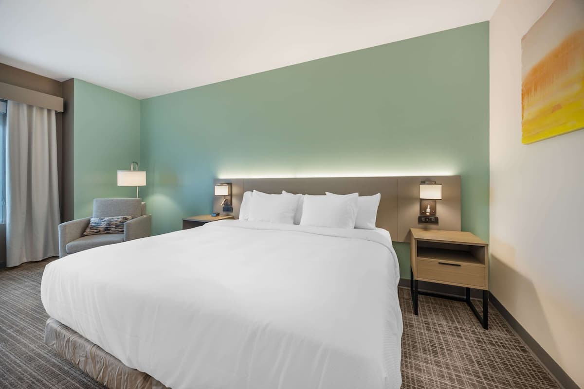 Une chambre d’hôtel avec un grand lit, deux tables de chevet avec des lampes, une chaise et un tableau au mur.