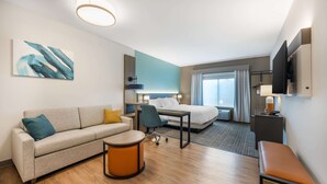 Ein modernes Hotelzimmer mit einer Couch, einem kleinen runden Tisch, einem Schreibtisch, einem Bett und einem Fernseher.
