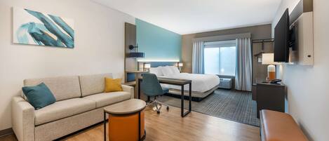 Ein modernes Hotelzimmer mit einer Couch, einem kleinen runden Tisch, einem Schreibtisch, einem Bett und einem Fernseher.