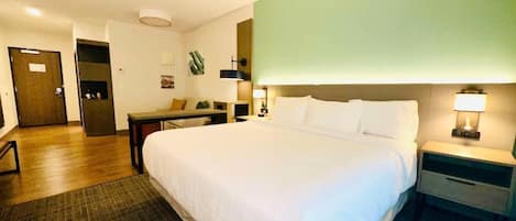 Quarto de hotel com uma cama grande, mesa de cabeceira, escrivaninha, cadeira e uma porta.