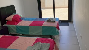 Quarto de hotel pequeno com duas camas, cada uma com roupa de cama colorida. Há uma janela com vista para um edifício.