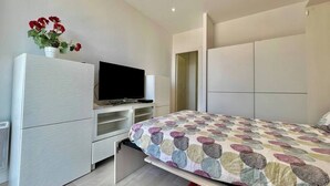 Ein Schlafzimmer mit einem Bett, einem Fernseher auf einem Schrank, einer Kommode und einer Tür zu einem anderen Raum.
