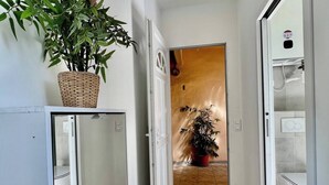 Ein schmaler Flur mit einem Blumentopf auf einem Standfuß, einer Tür zu einem Badezimmer und einem weißen Schrank mit Spiegel.