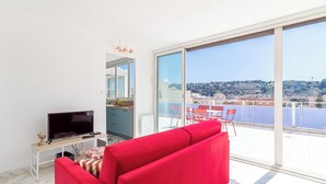 A modern living room with a red sofa, a TV on a wooden stand, and a balcony with a view of the city. - Superb  Rooftop Roquebrune Parking (Roquebrune-Cap-Martin)