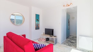 A modern living room with a red sofa, a TV on a wooden stand, and a view of the city through a window. - Superb  Rooftop Roquebrune Parking (Roquebrune-Cap-Martin)