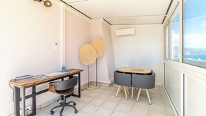 A small, well-lit room with a wooden desk, black office chair, two round tables, and a large window offering a view. - Superb  Rooftop Roquebrune Parking (Roquebrune-Cap-Martin)