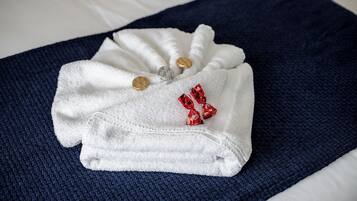 A neatly folded white towel with two gold and one silver towel ring, and three red candies on a dark blue textured fabric.