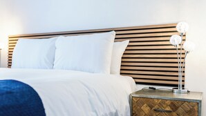 A neatly made bed with white linens and a blue throw blanket, a wooden headboard, and a bedside table with a decorative lamp. - Cosy 2-bed Apartment in Nettleham (Lincoln)