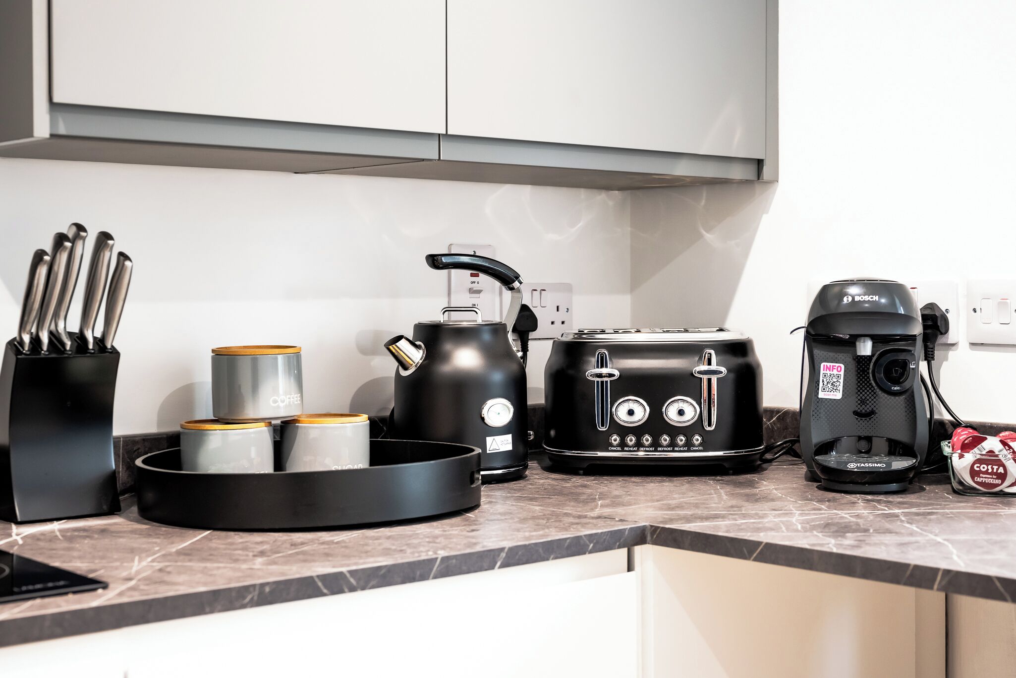 A kitchen with a coffee maker, toaster, kettle, and coffee cups on the counter.