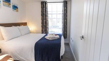 A hotel room with a bed, a window with curtains, a bedside table, and a wall-mounted light.