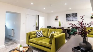 A modern living room with a green sofa, a dining area, and a kitchen in the background. - Cosy 2-bed Apartment in Nettleham (Lincoln)