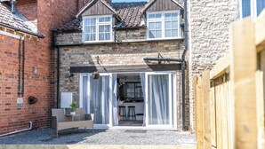 Une maison avec une façade en briques, un petit jardin et un patio comprenant un banc et une table.