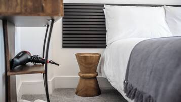 A neatly made bed with white linens and a gray blanket, a wooden bedside table with a power outlet, and a black headboard.