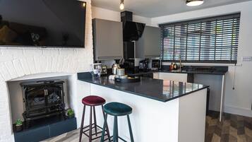 A modern kitchen with a central island, bar stools, a built-in stove, and a large window with blinds.
