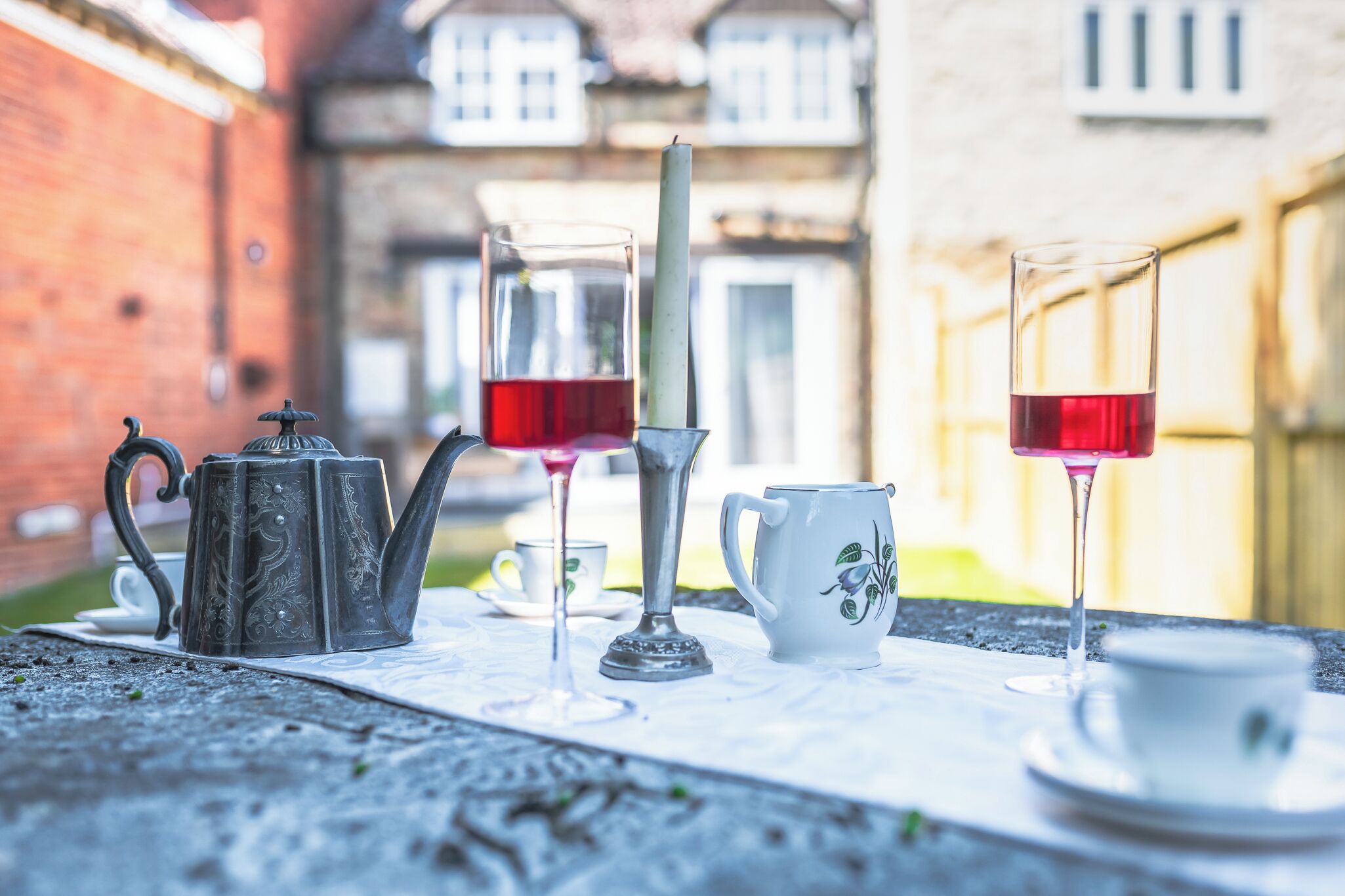 Une table dressée avec une théière, une bougie, un pichet et deux verres contenant un liquide rouge, vraisemblablement du thé, le tout posé sur une nappe.