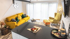 Un salon moderne avec un canapé jaune, un fauteuil à motifs et une table basse sur laquelle sont disposés des en-cas.