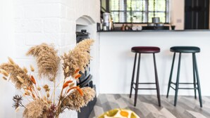 Une cuisine moderne avec un mur en briques blanches, une fenêtre avec des stores et deux tabourets de bar.