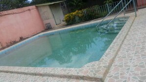 A rectangular swimming pool with a stone tiled edge, surrounded by a metal fence and a pink wall.