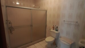 A bathroom with a shower, toilet, and a shelf with toiletries.